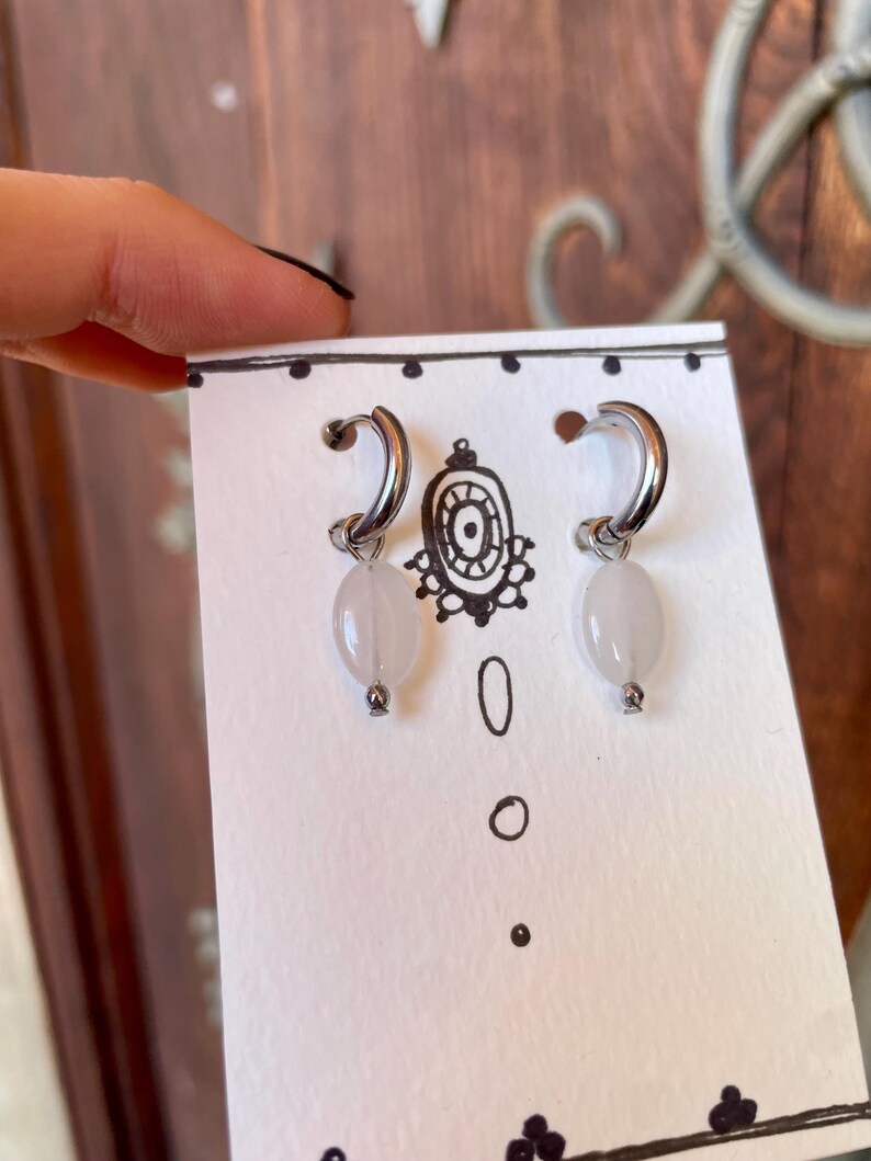 May include: A pair of silver hoop earrings with a white oval-shaped stone hanging from each hoop.