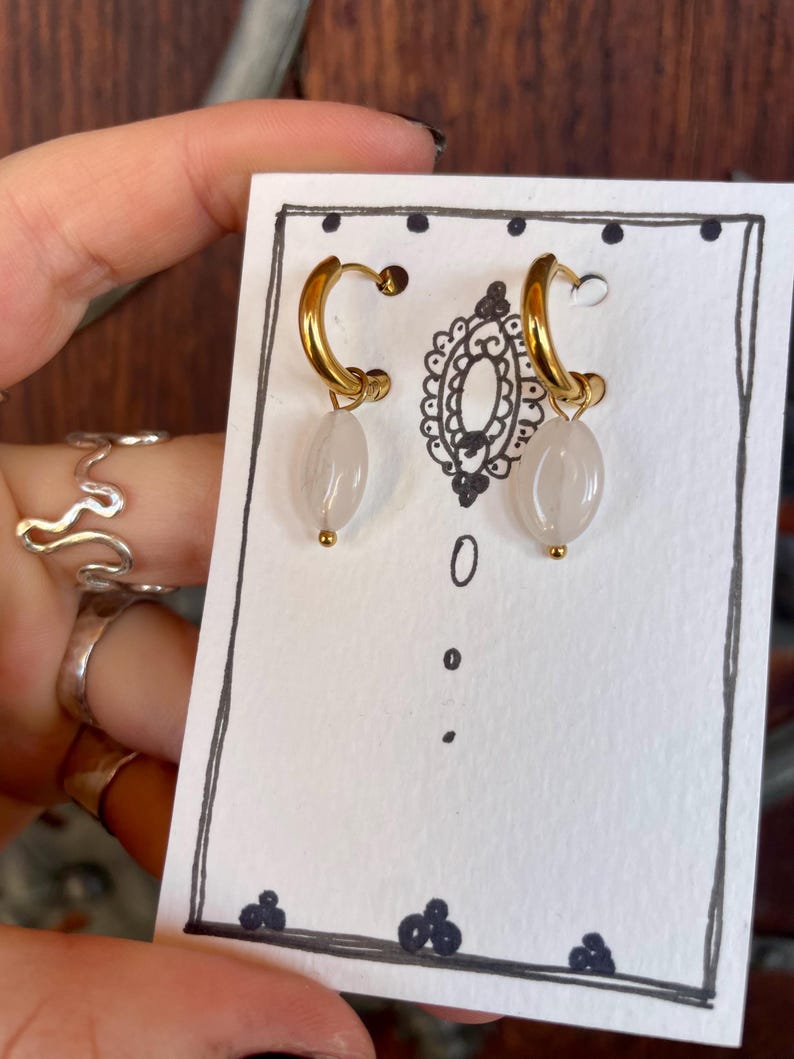 May include: A pair of gold hoop earrings with a white stone pendant hanging from each hoop.