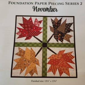 May include: A Foundation Paper Piecing Series 2 November quilt pattern featuring four maple leaf blocks in red, brown, yellow, and orange fabric prints, separated by a green cross-shaped sashing. The finished size is 13.5 inches by 13.5 inches.