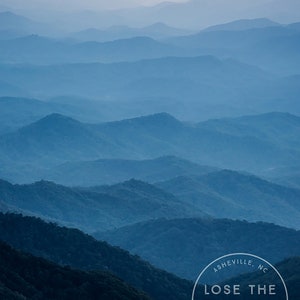 Peut inclure: Un logo bleu et blanc avec le texte "Lose the Trail" dans un cercle avec les mots "Asheville, NC" et "Find Adventure" en dessous. Le logo est superposé sur une photographie d'une chaîne de montagnes avec un ciel bleu brumeux.