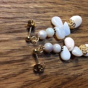 May include: A pair of dangle earrings with white and iridescent stones and gold accents.