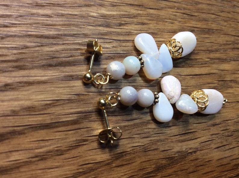 May include: A pair of dangle earrings with white and iridescent stones and gold accents.