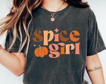 May include: Dark gray t-shirt with the text "Spice Girl" in brown, orange, and pink lettering, and a pumpkin graphic. The shirt is worn with blue jeans and white sneakers. The overall theme is fall and autumn.