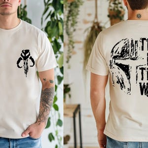 Puede incluir: Camiseta beige con un gr&aacute;fico negro en la parte delantera y trasera. La parte delantera presenta un dise&ntilde;o de calavera estilizado. La parte trasera muestra un gr&aacute;fico de casco y el texto "THIS IS THE WAY".