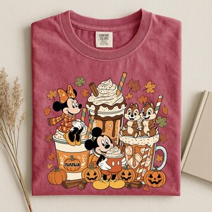 Pu&ograve; includere: Una t-shirt girocollo color bordeaux con una stampa di Minnie, Topolino e Cip e Ciop con bevande a tema autunnale. Il design include zucche, bastoncini di cannella e foglie autunnali. Presenta un'etichetta del marchio Comfort Colors.