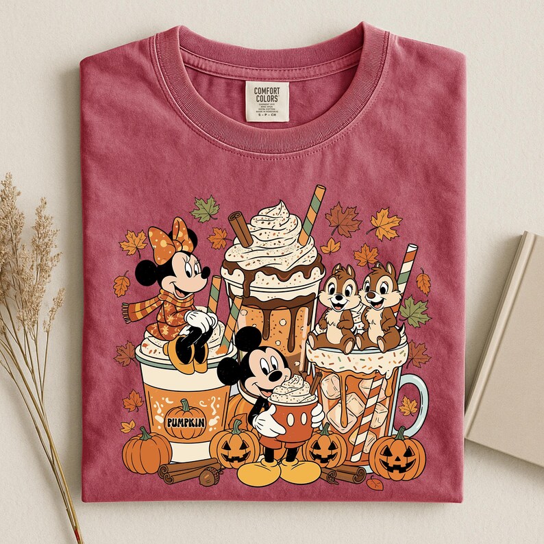 Pu&ograve; includere: Una t-shirt girocollo color bordeaux con una stampa di Minnie, Topolino e Cip e Ciop con bevande a tema autunnale. Il design include zucche, bastoncini di cannella e foglie autunnali. Presenta un'etichetta del marchio Comfort Colors.