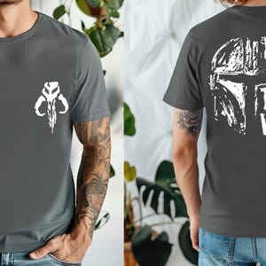 Puede incluir: Camiseta gris oscuro con un emblema de calavera mandaloriana blanca en la parte delantera y la frase "THIS IS THE WAY" con un gr&aacute;fico de casco en la espalda. La camiseta es de cuello redondo y manga corta.
