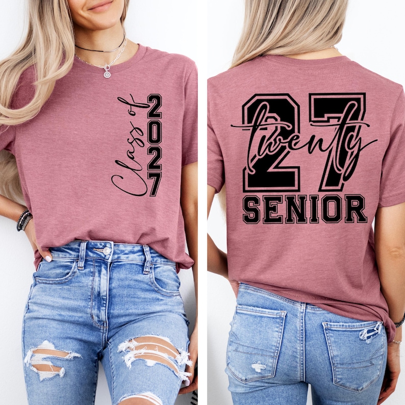 May include: A mauve-colored t-shirt with the text "Class of 2027" printed vertically on the front. The back of the shirt features the text "27 Twenty Senior" in a black, bold font. The shirt is paired with blue jeans.