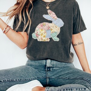 Puede incluir: Camiseta gris oscuro con un dise&ntilde;o de conejo de retazos. El conejo est&aacute; hecho de telas florales, de cuadros y de lunares en colores pastel. La camiseta se combina con vaqueros azules y zapatos blancos.
