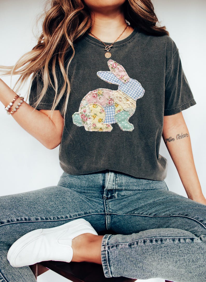 Puede incluir: Camiseta gris oscuro con un dise&ntilde;o de conejo de retazos. El conejo est&aacute; hecho de telas florales, de cuadros y de lunares en colores pastel. La camiseta se combina con vaqueros azules y zapatos blancos.