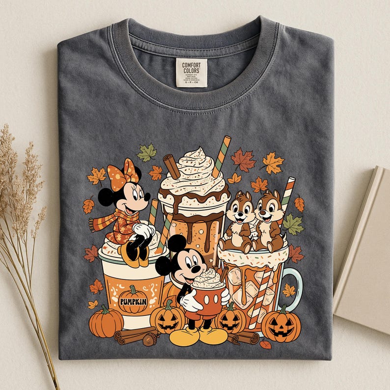 Pu&ograve; includere: Una t-shirt grigio antracite con una stampa grafica di Minnie, Topolino e Cip e Ciop con bevande a tema autunnale, zucche e foglie cadenti. La maglietta presenta un'etichetta del marchio Comfort Colors all'interno del colletto.
