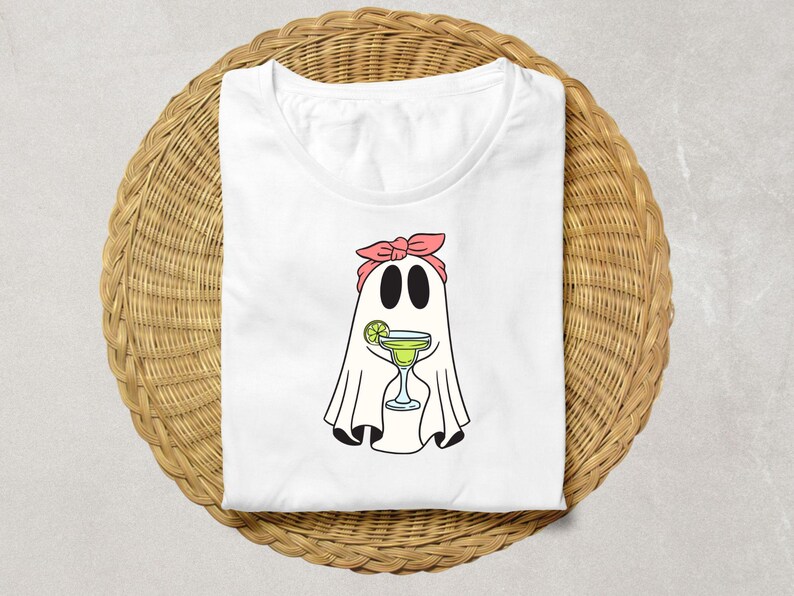 Pu&ograve; includere: Maglietta bianca con un fantasma dei cartoni animati che indossa un bandana rosa e tiene un bicchiere di margarita. Il fantasma ha uno spicchio di lime nel suo bicchiere.