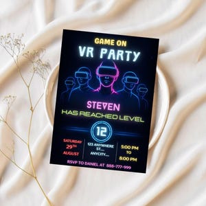 Puede incluir: Tarjeta de invitaci&oacute;n negra con texto y gr&aacute;ficos de ne&oacute;n para una fiesta de realidad virtual. La tarjeta presenta el texto "GAME ON VR PARTY" y "STEVEN HAS REACHED LEVEL". Detalles de fecha, hora e informaci&oacute;n de confirmaci&oacute;n de asistencia. La tarjeta est&aacute; sobre un plato blanco.