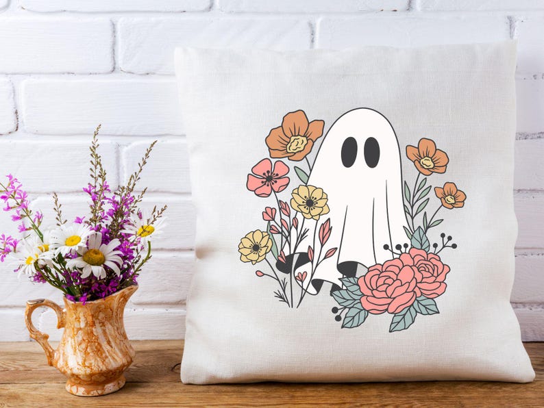 Pu&ograve; includere: Un cuscino bianco con un fantasma e fiori stampati su di esso. Il fantasma &egrave; bianco con due occhi neri ed &egrave; circondato da fiori rosa, arancioni e gialli.