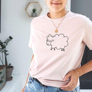 May include: A pink t-shirt with a black and white cartoon sheep graphic.