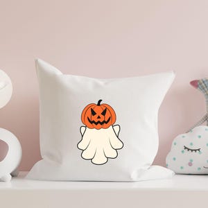 Pu&ograve; includere: Un cuscino bianco con un fantasma che indossa una zucca intagliata come testa. Il fantasma &egrave; bianco e la zucca &egrave; arancione con un viso nero.