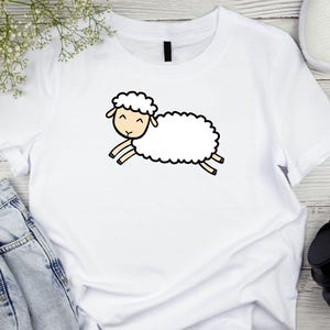 May include: White t-shirt with a cartoon illustration of a white sheep with black eyes and a smile.