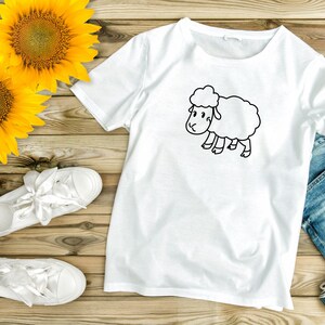 May include: White t-shirt with a black line drawing of a sheep on a wooden background with sunflowers and white sneakers.