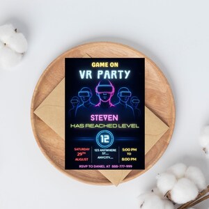 Puede incluir: Una tarjeta de invitaci&oacute;n negra con texto y gr&aacute;ficos en ne&oacute;n azul y rosa para una fiesta de realidad virtual. La tarjeta incluye el texto "GAME ON VR PARTY", "STEVEN HAS REACHED LEVEL" y los detalles del evento. La tarjeta est&aacute; sobre un plato de madera con un sobre.