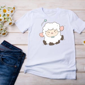 May include: White t-shirt with a cartoon illustration of a white lamb with a blue bow tie. The lamb is smiling and has a star above its head.