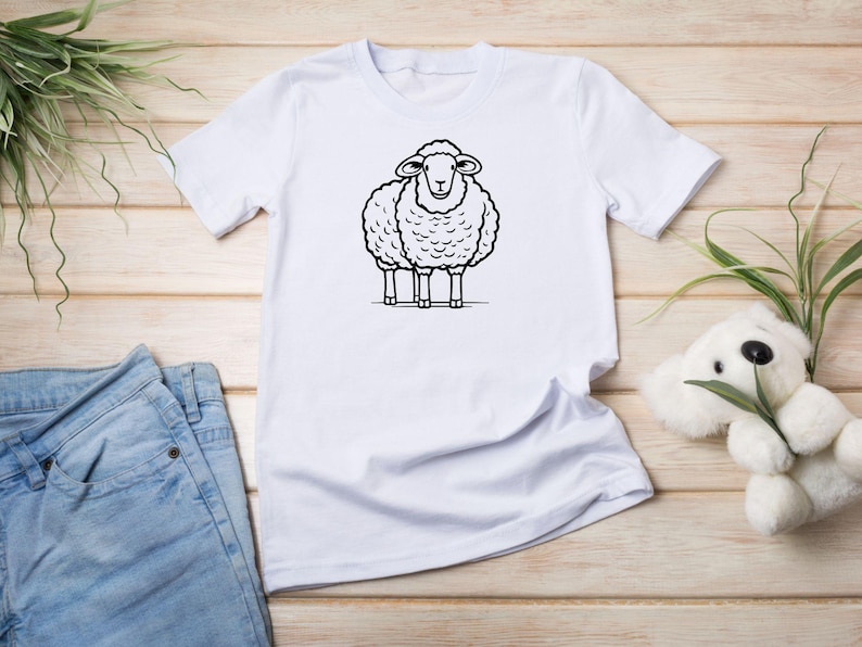 May include: White t-shirt with a black and white cartoon sheep illustration.