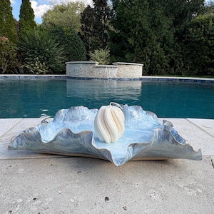 May include: A light blue and white marbled ceramic tray with a wavy, organic edge. Centered on the tray is a white, spiraled, pumpkin-shaped candle with a single wick. The tray has a glossy finish with subtle color variations.
