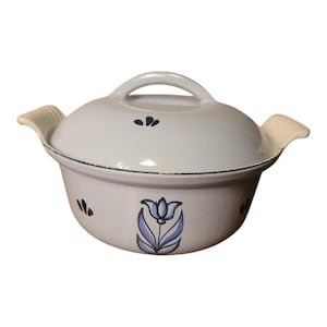 May include: A light gray ceramic casserole dish with a matching lid, featuring a hand-painted blue tulip motif on the front and small dark blue leaf accents. The pot has two side handles with a ribbed texture and a dark rim along the edge.