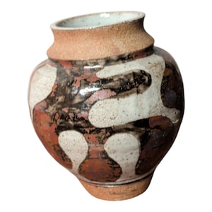May include: A ceramic vase with a rounded body and a narrow neck. The exterior features a mottled glaze pattern in shades of cream, dark brown, and terracotta red. The rim and base are finished in an unglazed, textured, light brown clay finish.