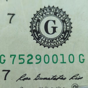 May include: Close-up of a U.S. dollar bill with the Federal Reserve seal, the letter "G", and the words "Chicago, Illinois." The serial number "G 75290010 G" is printed in green.