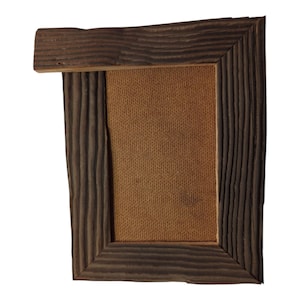 May include: A rustic, rectangular picture frame with a dark brown, textured wood finish. The frame has a natural, unfinished look with visible wood grain and a light brown backing. The top of the frame extends outward.