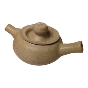 May include: A tan ceramic teapot with a lid and a small knob on top. The teapot has a rounded body, a spout, and a handle. The ceramic has a speckled appearance.