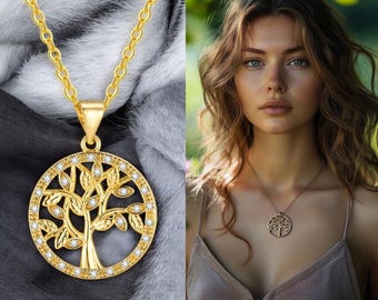 May include: A gold-colored necklace featuring a pendant with a tree of life design. The pendant is circular, with a detailed tree motif and small, clear stones around the edge. The chain is also gold-colored, and the necklace is displayed on a soft, gray background.