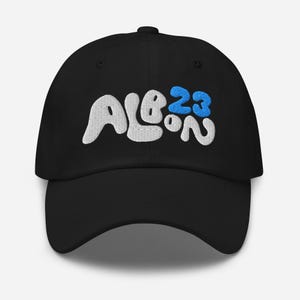 Pode incluir: Boné de beisebol preto com texto bordado em branco que diz "ALBO 23" em uma fonte estilizada. O número "23" está em azul.
