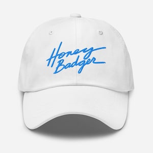 Puede incluir: Gorra de béisbol blanca con un logotipo bordado en azul que dice "Honey Badger".