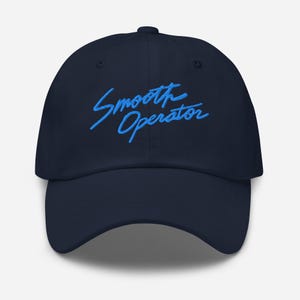 Puede incluir: Una gorra de béisbol azul marino con el texto "Smooth Operator" bordado en azul en la parte delantera.