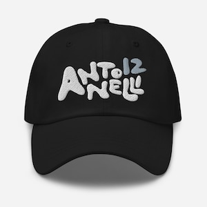 Pode incluir: Boné de beisebol preto com o texto bordado "ANTO12NELL" em branco e azul claro. O boné tem uma aba curva e uma coroa arredondada. Um acessório casual para uso diário.