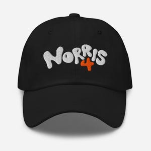 Pode incluir: Boné de beisebol preto com o texto "NORRIS 4" bordado em branco e o número 4 em laranja.