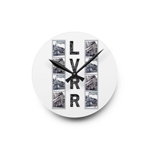 May include: A white round clock with black hands and a black and white image of a train engine repeated vertically. The letters LVRR are printed vertically in black.