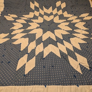 Puede incluir: Una colcha azul y blanca con un patrón de estrella. La colcha está hecha de tela de algodón y tiene un aspecto cosido a mano.