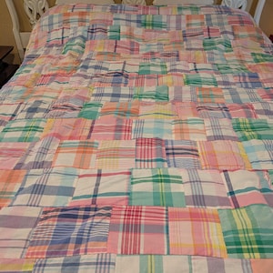 Könnte beinhalten: Ein Patchwork-Quilt mit verschiedenen pastellfarbenen Karomustern in Rosa, Blau, Grün und Gelb. Der Quilt liegt auf einem weißen Kopfteil und schafft eine gemütliche und farbenfrohe Bettwäsche.