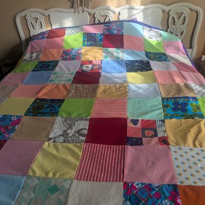Pode incluir: Uma colcha de retalhos colorida com uma variedade de padrões e cores de tecido, incluindo vermelho, azul, verde e amarelo. A colcha está sobre uma cabeceira branca. A colcha é uma mistura de quadrados e retângulos.