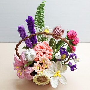 May include: A crocheted flower arrangement in a brown basket. The arrangement includes pink, white, purple, and yellow flowers, as well as green leaves.