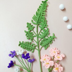 May include: A set of crocheted flowers and a fern. The flowers are pink, white, and purple. The fern is green.