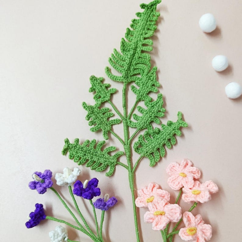 May include: A set of crocheted flowers and a fern. The flowers are pink, white, and purple. The fern is green.