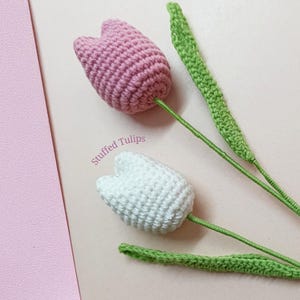 May include: Two crocheted stuffed tulips, one pink and one white, with green crocheted leaves. The text "Stuffed Tulips" is written on the image.