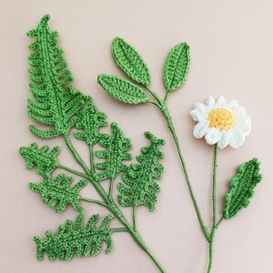May include: Crocheted green leaves and a white daisy with a yellow centre. The leaves are arranged in a cluster, while the daisy is on a separate stem.