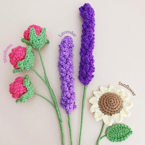 May include: A set of crocheted flowers, including mini roses, lavender, and a sunflower. The flowers are all different colours and are arranged in a row. The flowers are made with yarn and are very detailed.
