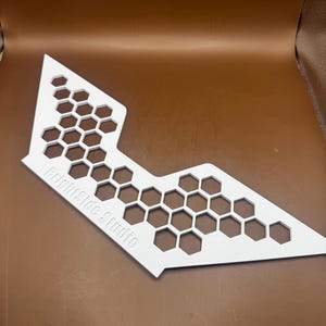 May include: A white, angular, flat object featuring a repeating honeycomb pattern of hexagonal cutouts. The text "Brightside Studio" is embossed in a sans-serif font on the lower left section of the white surface, which has a matte finish.