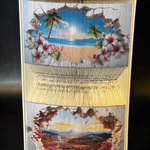 Może przedstawiać: Książka ze złożonymi stronami, tworząca trójwymiarowy obraz plaży z palmami i górskim krajobrazem. Książka jest otwarta, a strony są złożone, aby stworzyć efekt 3D.