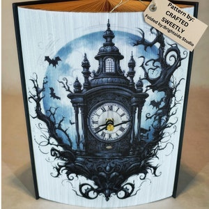 Op de afbeelding: Een boek gevouwen in de vorm van een klokkentoren met een volle maan en vleermuizen op de achtergrond. De klokkentoren is zwart-wit met een gouden wijzerplaat. De tekst op het label luidt "Pattern by: CRAFTED SWEETLY Folded by: Brightside Studio".